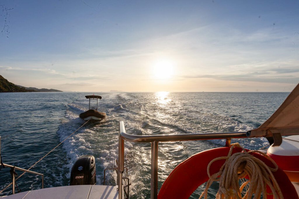 A dinghy being dragged by rope in front of a sunset